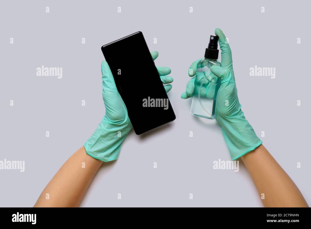 Female's hands in latex gloves wiping mobile phone with alcohol decontaminating agent top view over light grey background Stock Photo