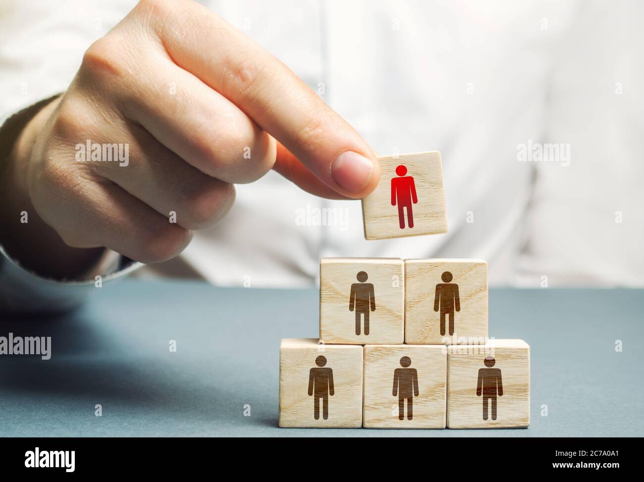 A hand places a mentor leader at the head of a group of people. Team building, hierarchical power vertical. Leadership skills. Teamwork, cooperation a Stock Photo