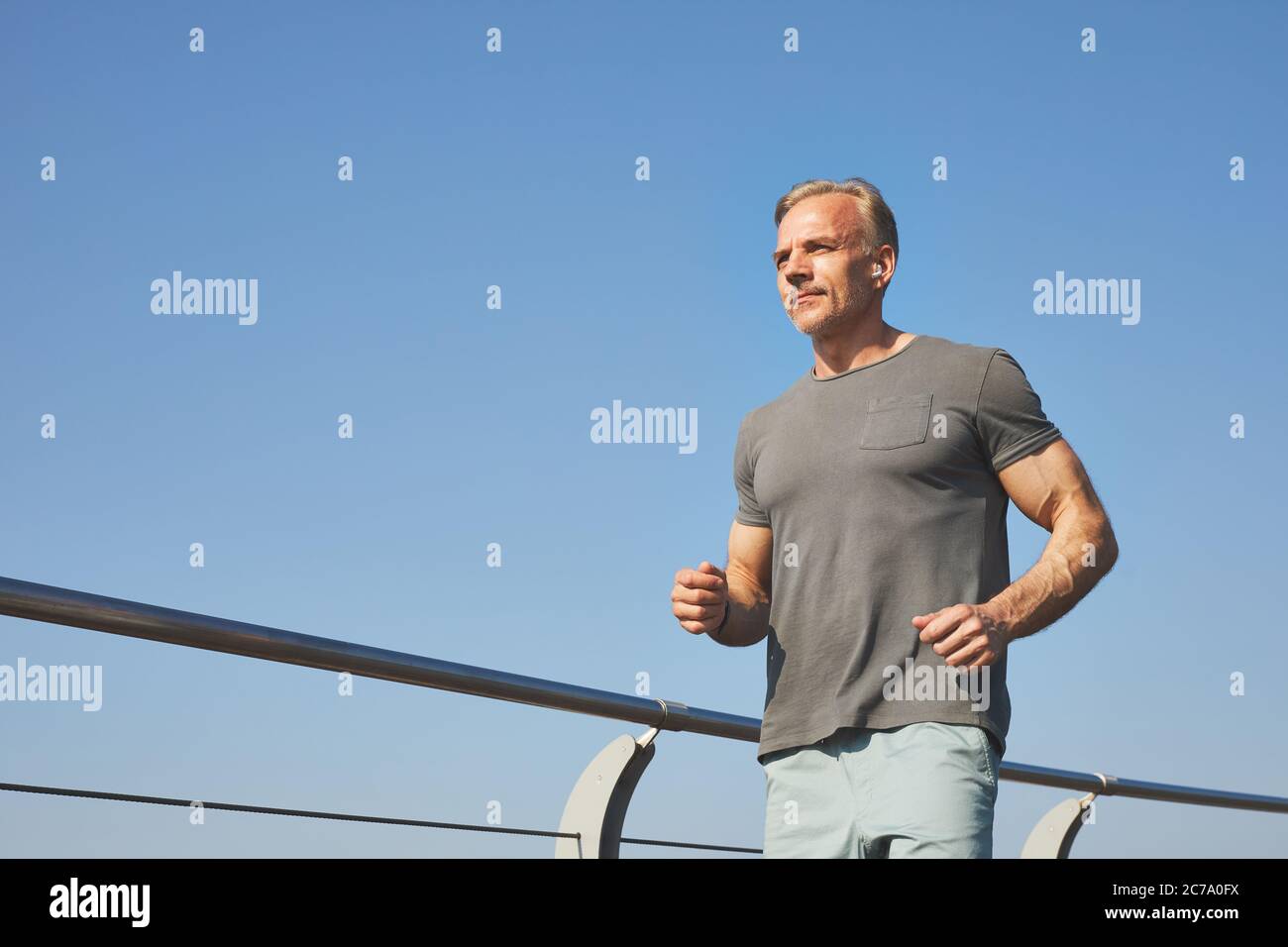 Below view of content active mature man in gray tshirt bending arms and running outdoors Stock Photo