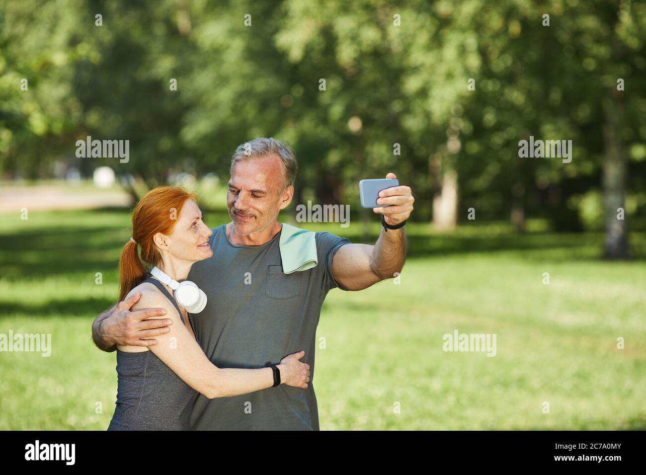 Loving mature couple looking at each other and embracing while posing for selfie in park after sports training Stock Photo