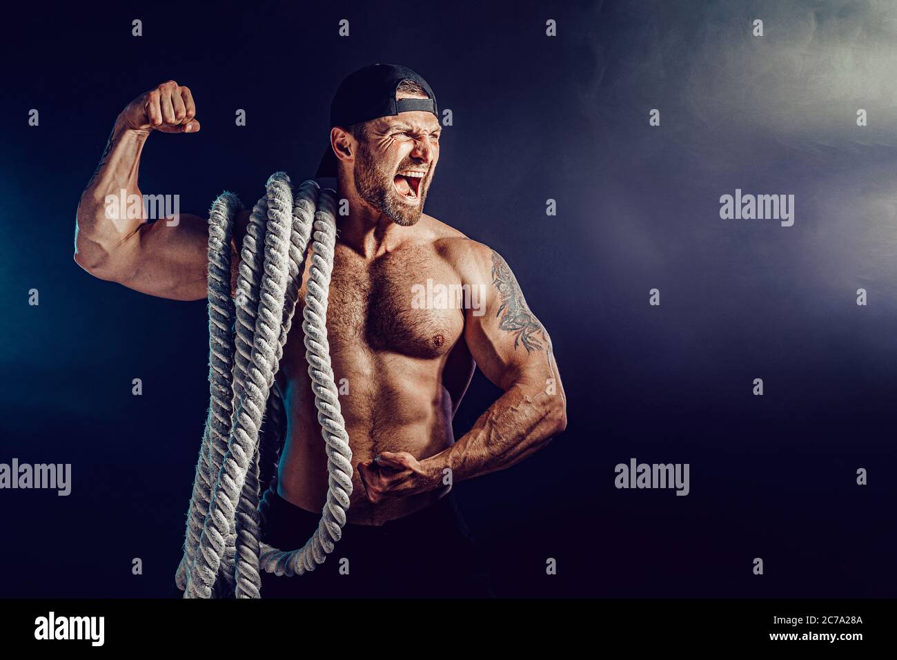 Muscular Arm Rope Aggressive bearded muscular sportsman holding battle rope on dark ...