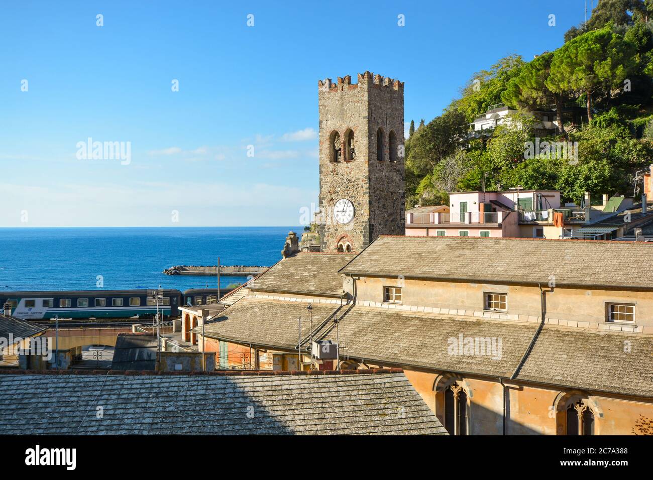 The tower of Chiesa di San Giovanni Battista with the Ligurian sea beyond as a train passes in Monterosso al Mare, Cinque Terre Italy on a sunny day Stock Photo
