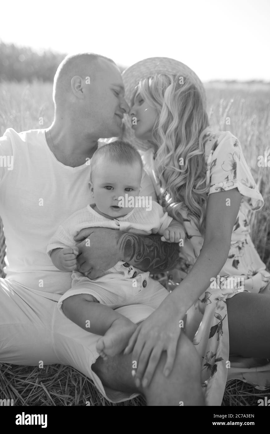 Happy young parents with baby rests among wheat field and they kisses. Black and white image. Stock Photo