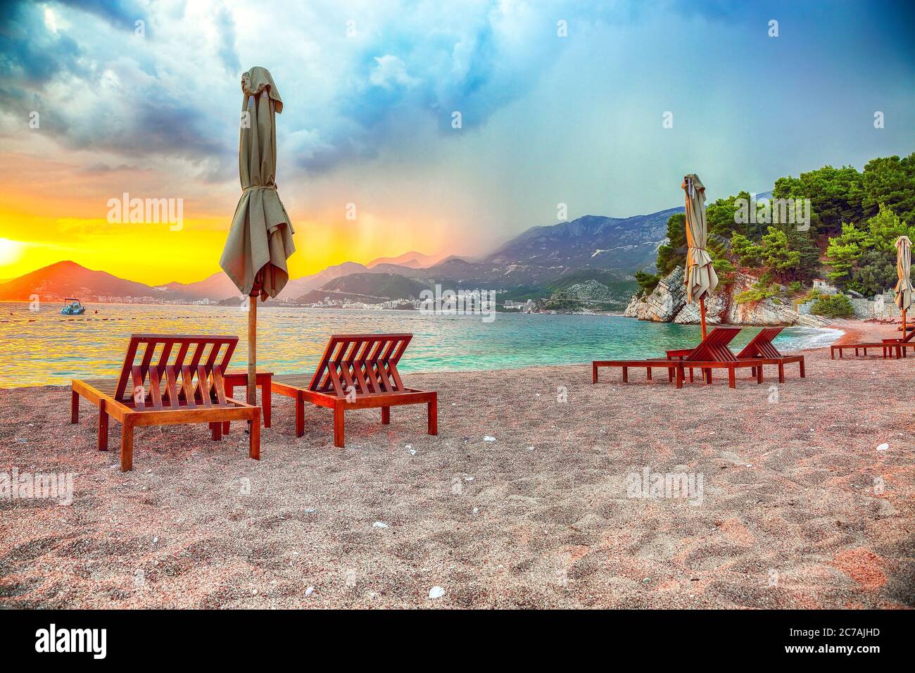 Dramatic sunset at beach with chaise lounges and umbrellas in Sveti Stefan near Budva.  Location:  Budva riviera, Montenegro, Adriatic sea, Europe Stock Photo