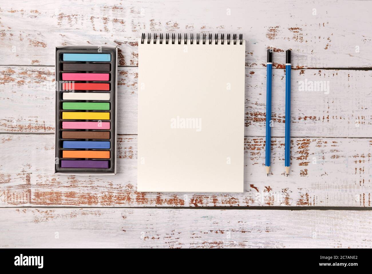 Colored wax crayons, pencils and white sketchbook on wooden background ...