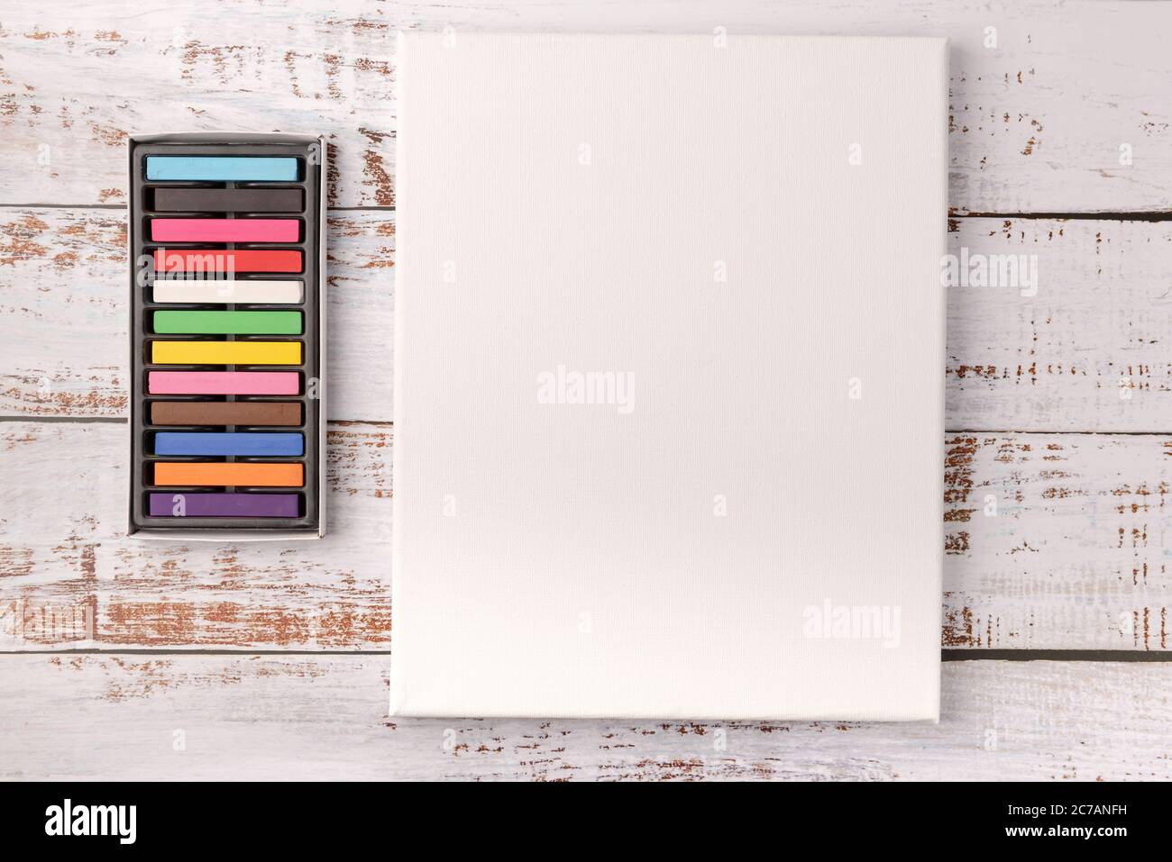 Colored wax crayons and white canvas on wooden background. Copy space ...