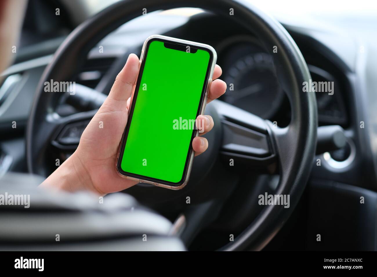 over shoulder of man holding green screen smart phone in the car. blur background Stock Photo