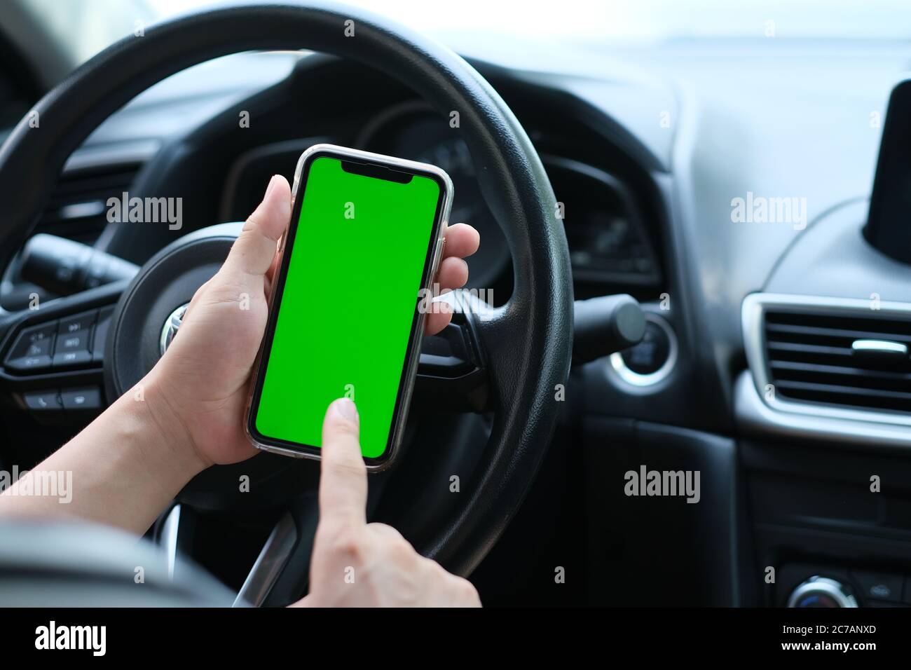 over shoulder of man tapping green screen smart phone in the car. blur background Stock Photo