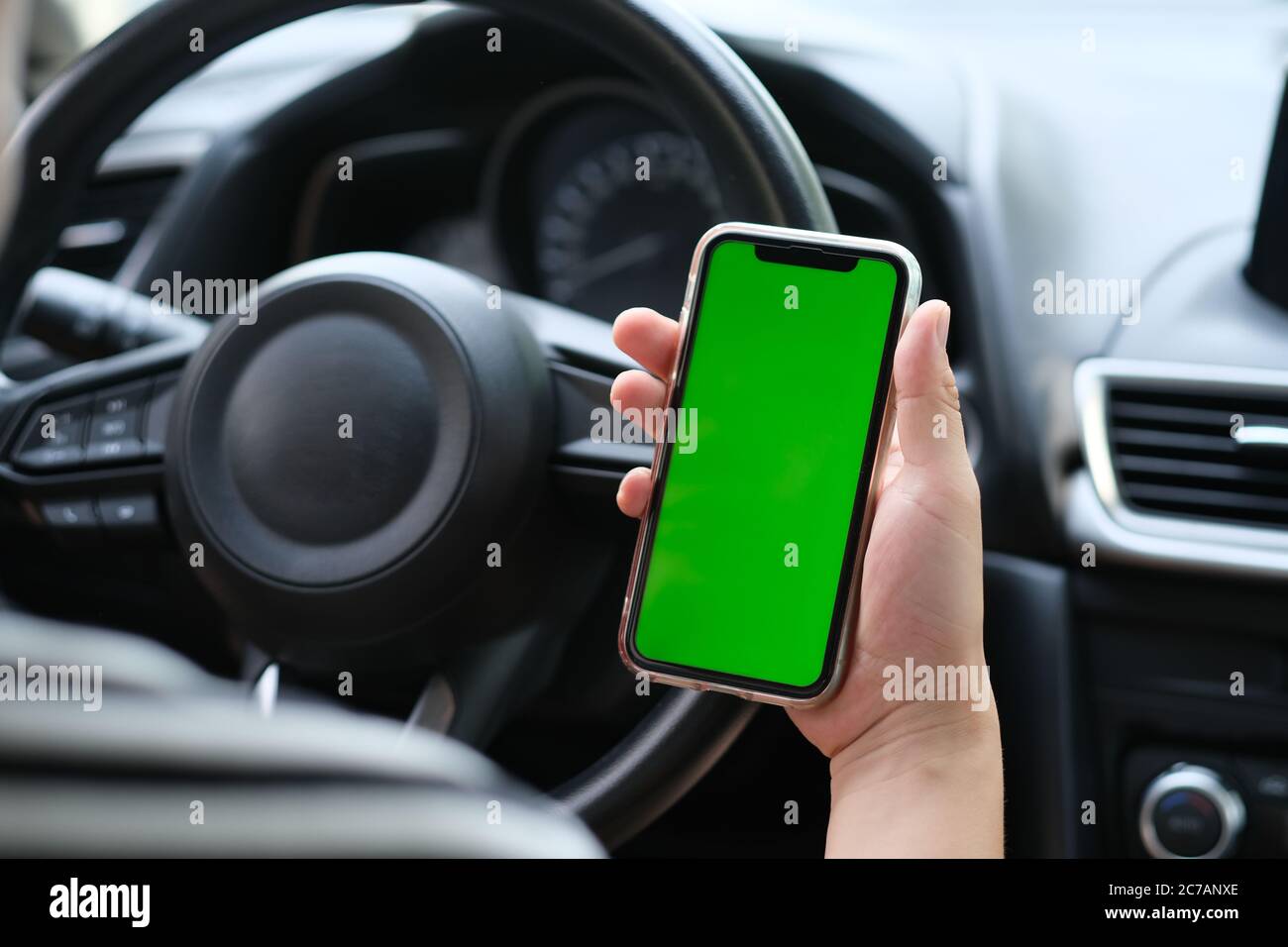 over shoulder of man holding green screen smart phone in the car. blur background Stock Photo