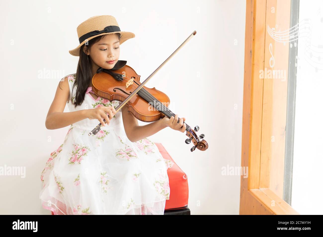 A cute Asian elementary school girl is playing a violin happily in her ...