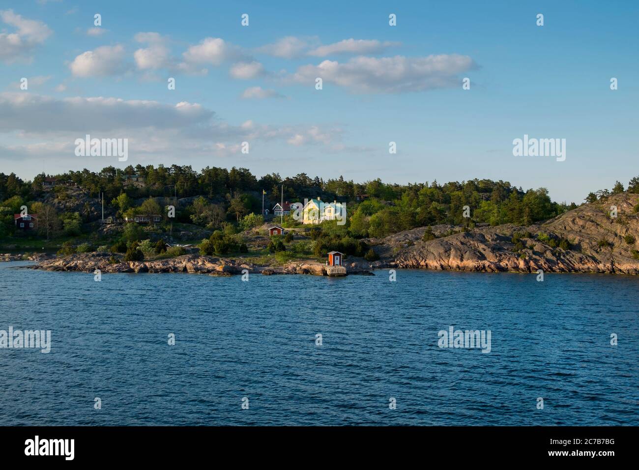 A small, red dockhouse sits on the coastline during late afternoon golden sunset. Cruising Lake Mälaren near Stockholm, Sweden. Stock Photo