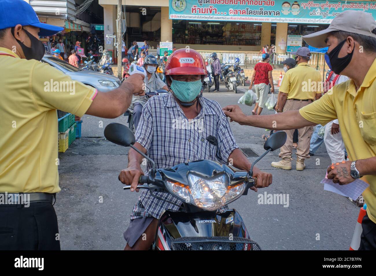 As a Covid-19 measure, to enter the wet market in Phuket Town, Thailand, visitors' temperature is checked and on being okayed get a colored sticker Stock Photo