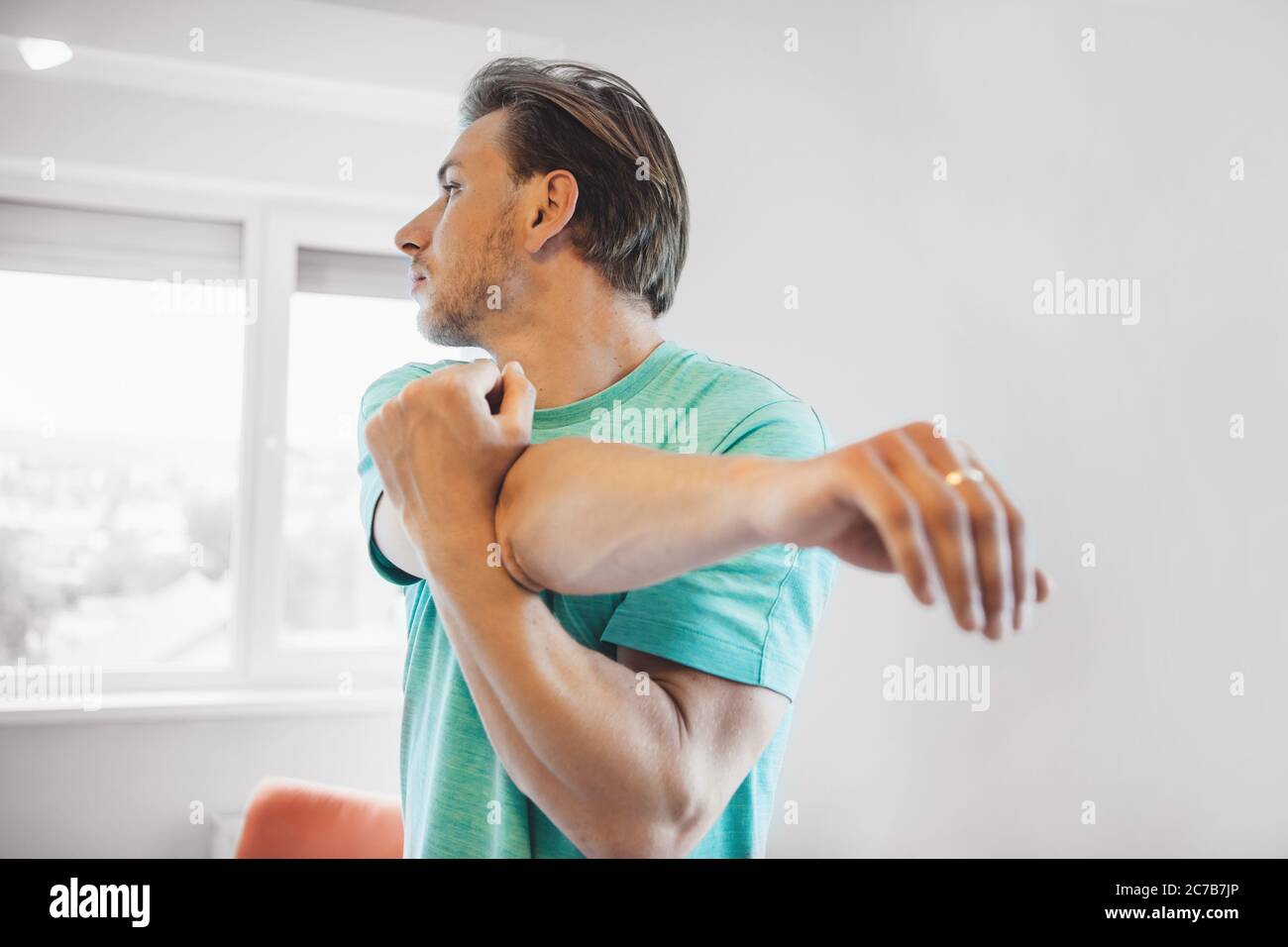 Close up photo of a caucasian man with blonde hair and bristle warming up before doing yoga at home Stock Photo