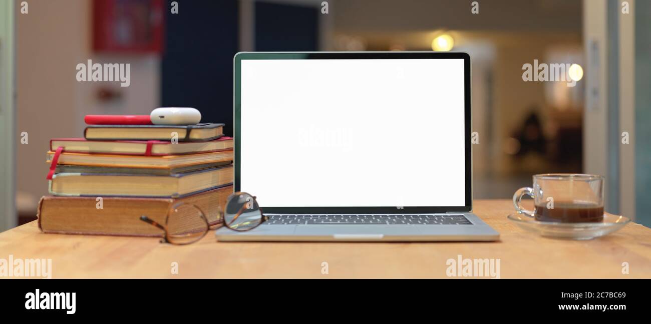 Close up view of study table with stack of books, mock up laptop, smartphone, glasses and coffee cup on wooden table Stock Photo