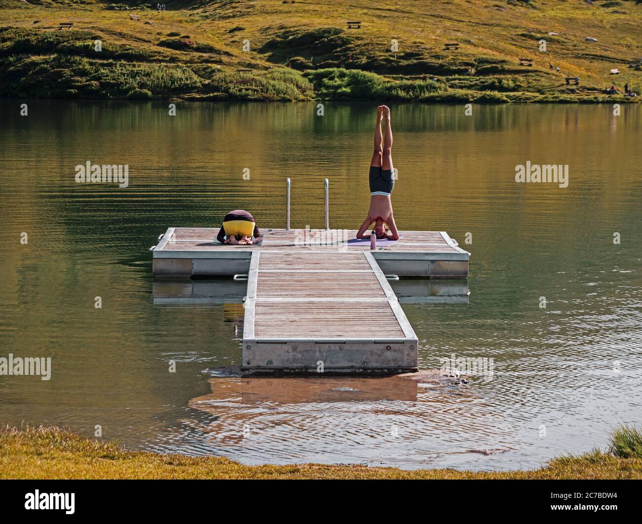 Bettmeralp, Valais, Switzerland - 07 15 2020: 2 women perform their morning yoga routine on a floating platform on a alpine lake. Stock Photo