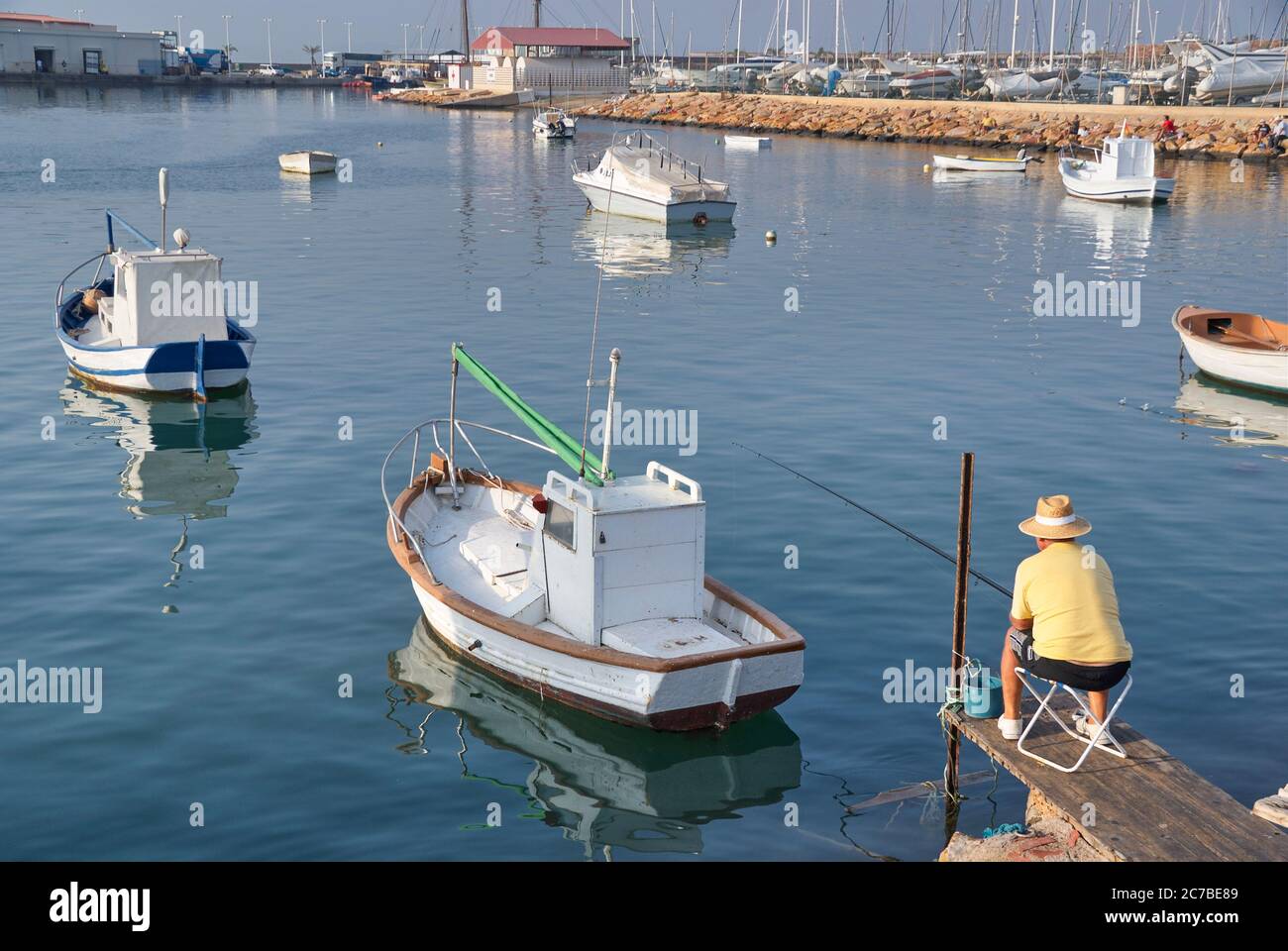 man in yellow shirt fishing in the mediterranean sea surrounded by small fishing boats. Spain Stock Photo