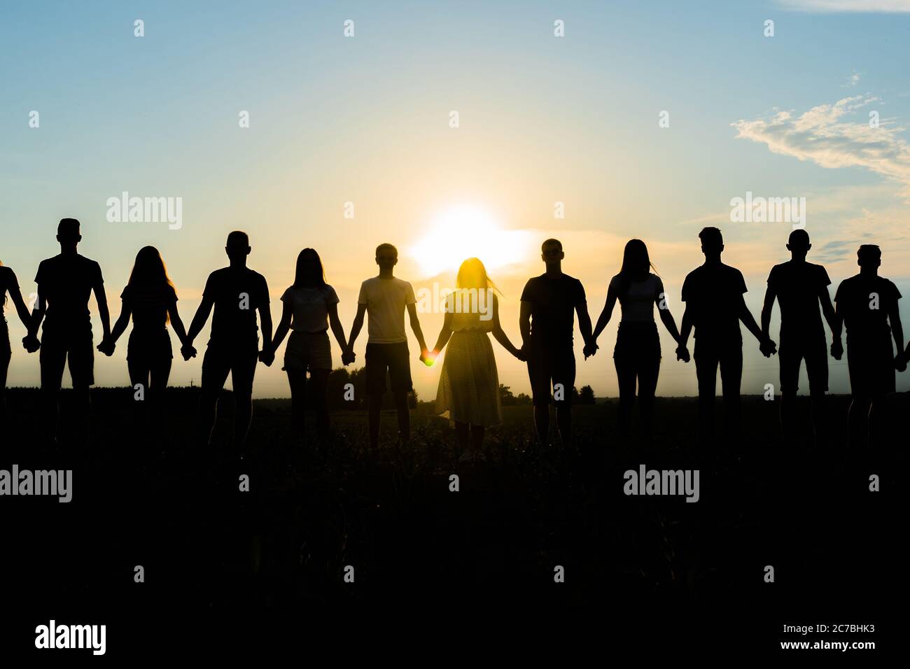 Cohesion concept. Black silhouettes of friends holding hands stands at sunset. Stock Photo