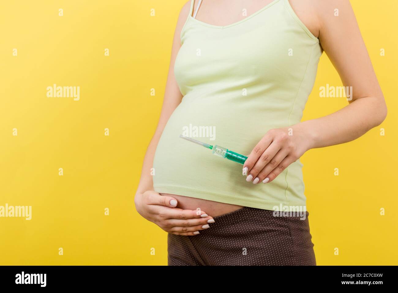 Close up of syringe for injection in pregnant woman's hand at colorful