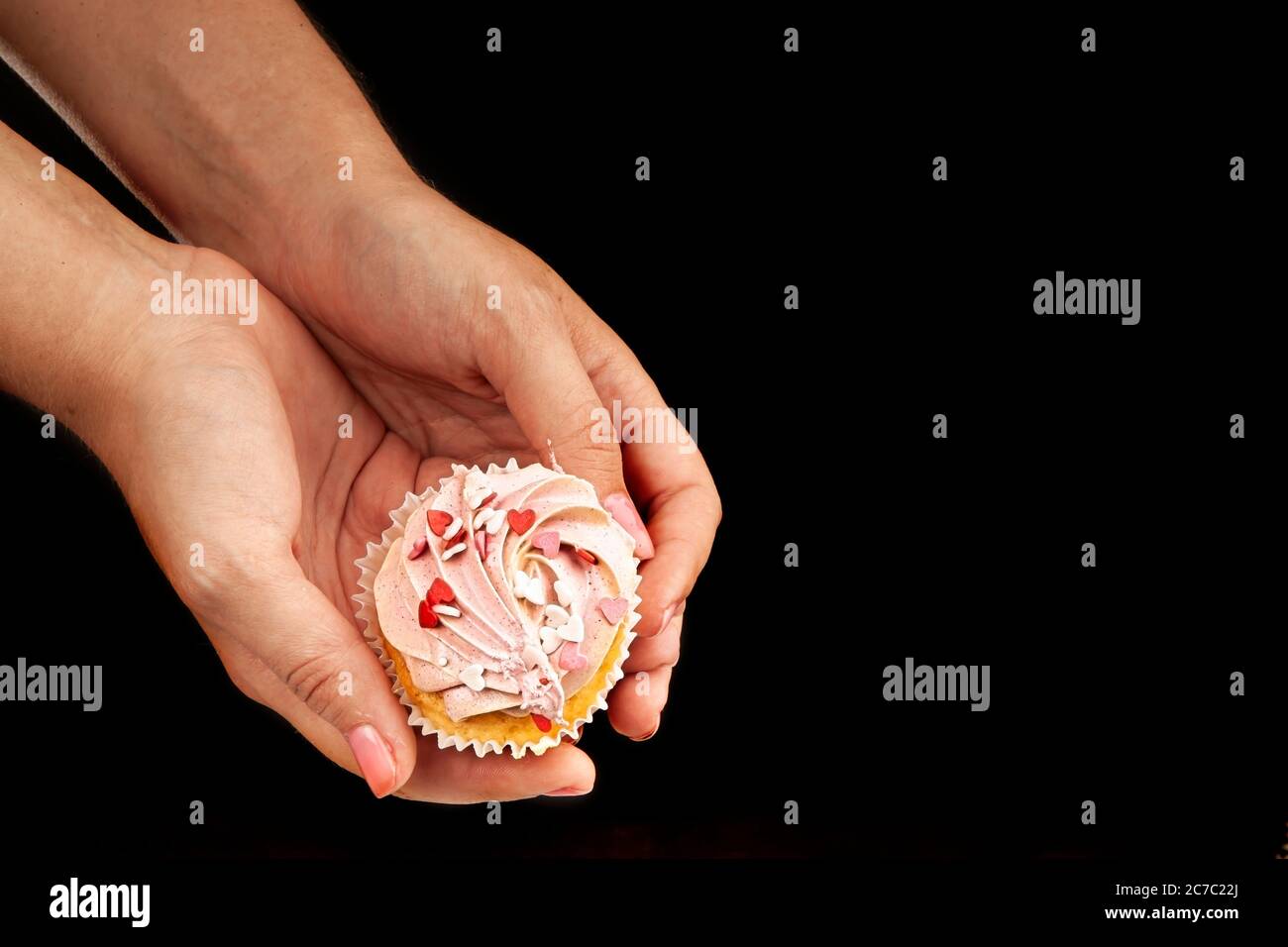 Female hands hold an appetizing, beautiful cupcake on a black background. Unhealthy, sweet food concept. Stock Photo