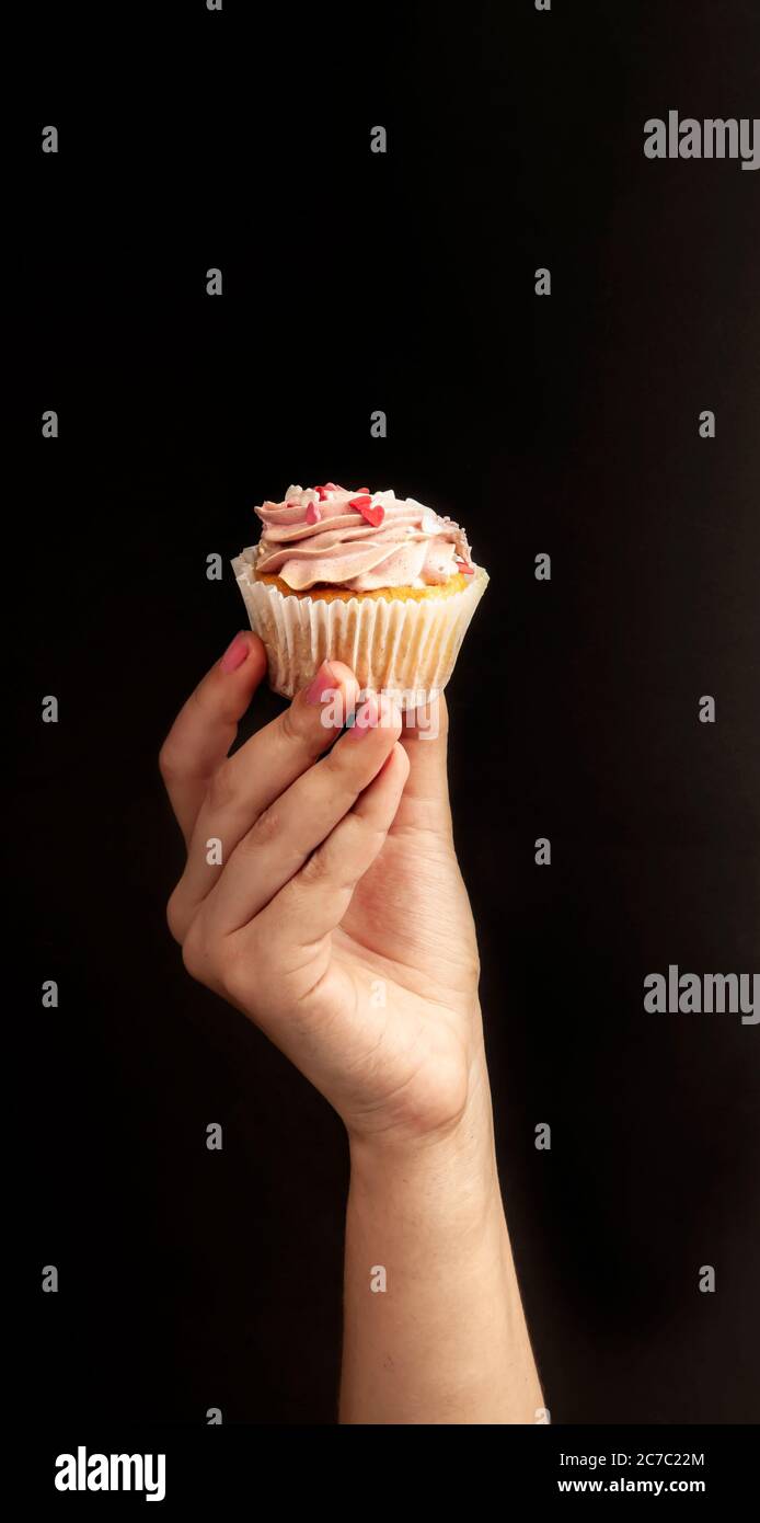 Female hands hold an appetizing, beautiful cupcake on a black background. Unhealthy, sweet food concept. Stock Photo