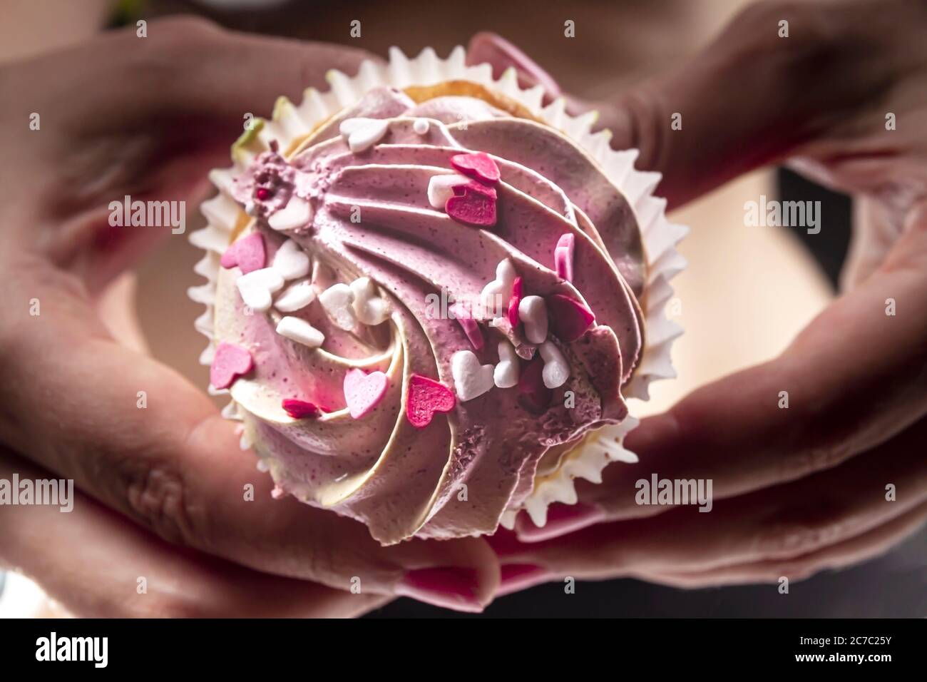 Female hands hold a sweet, appetizing cupcake against the background of a flat, toned female belly, and a thin waist. Unhealthy small amounts of sweet Stock Photo