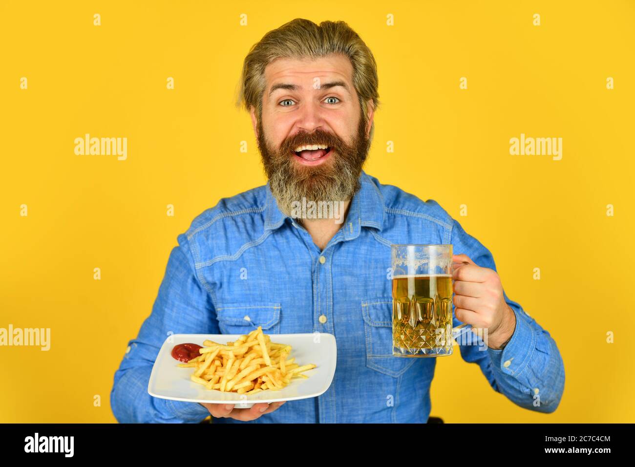 beer and french fries in restaurant. eating and drinking at bar. hipster relax in tavern. bearded guy having snack. lazy man enjoying fresh beer and junk food. man with fast food. Stock Photo