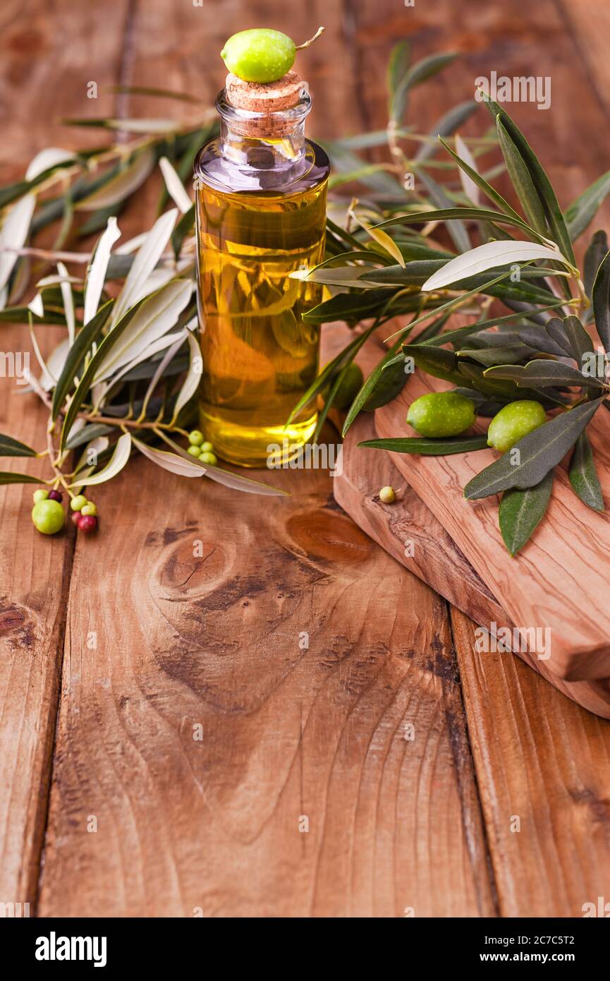 Green olives in tin cans with loaf of fresh bread and young olives branch , bottle of olive oil on clay board over old wood background. space for text  Stock Photo