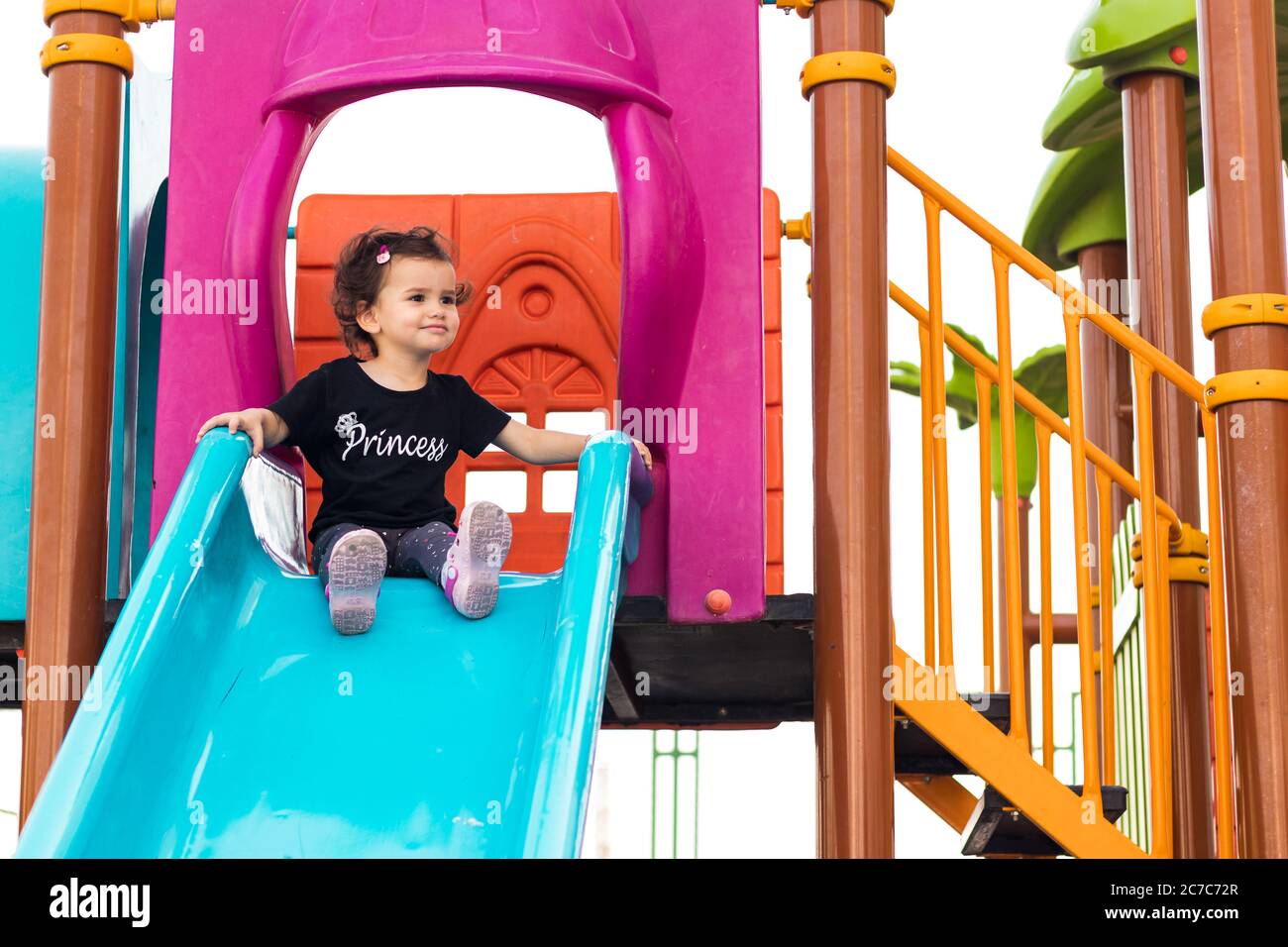 a cute liitle girl sitting on the blue slide in a playground Stock ...