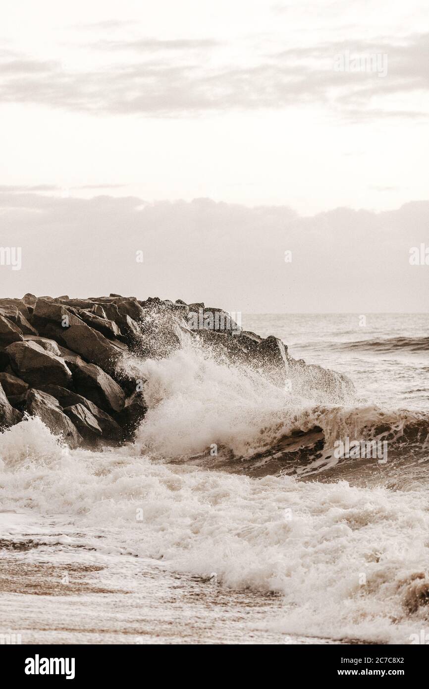 Vertical shot of waves splashing onto the rocky shore during daytime ...