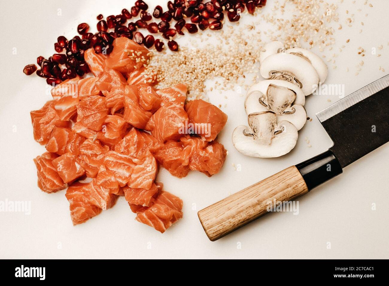 Closeup shot of a cutting board with fish, mushrooms, pomegranate seeds, and a knife on it Stock Photo