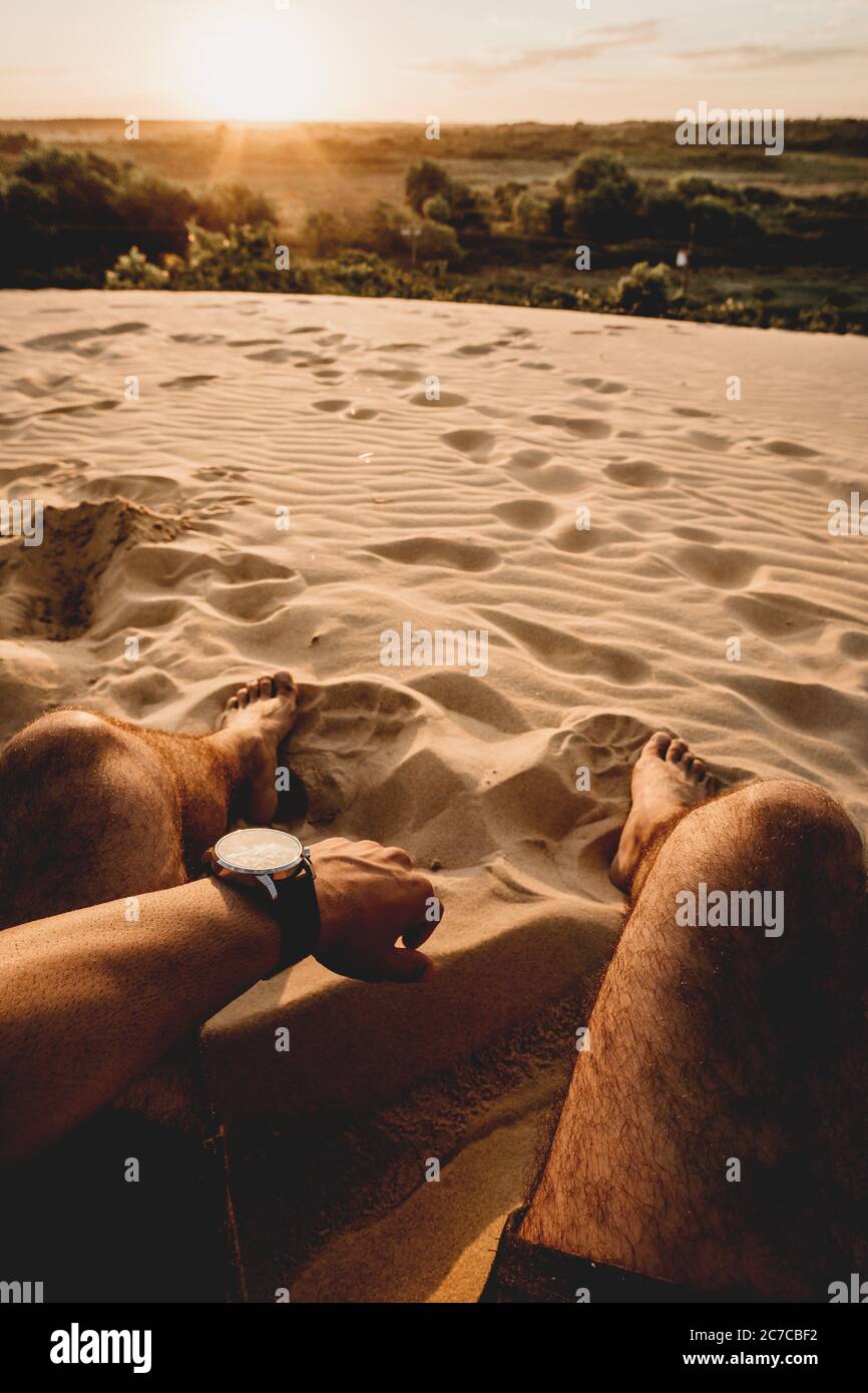Vertical shot of a sandy area with a man's legs and left hand visible in the shot during daytime Stock Photo