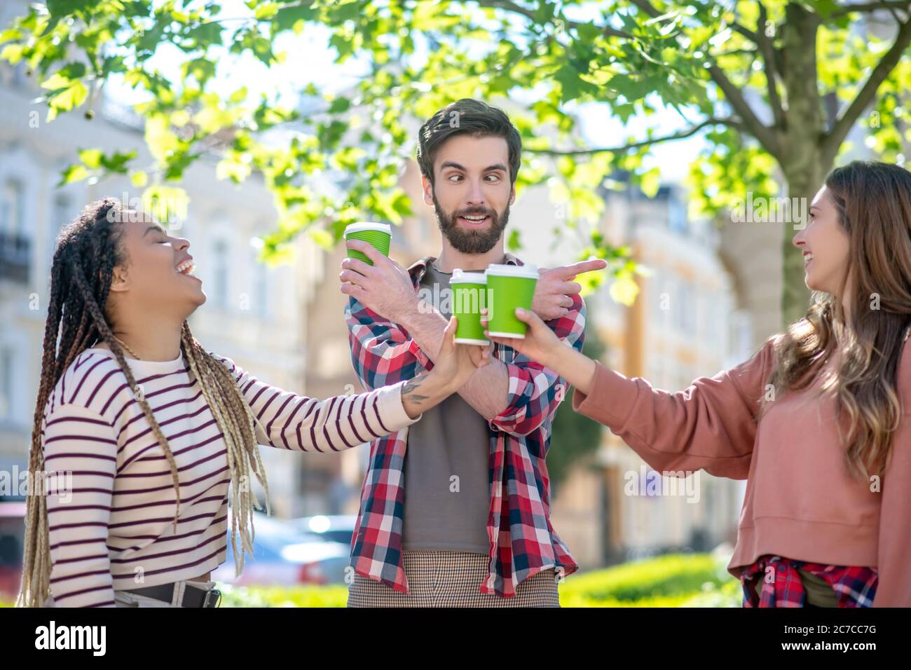 Joking cross-eyed guy and two laughing girls standing on street Stock Photo