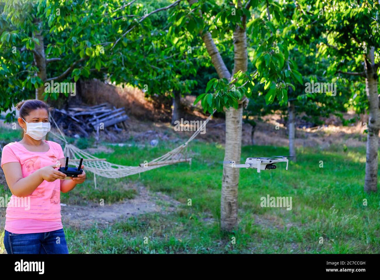 Woman flying drone in nature in new normal life. Woman having fun in the park with mask due to corona virus. Stock Photo