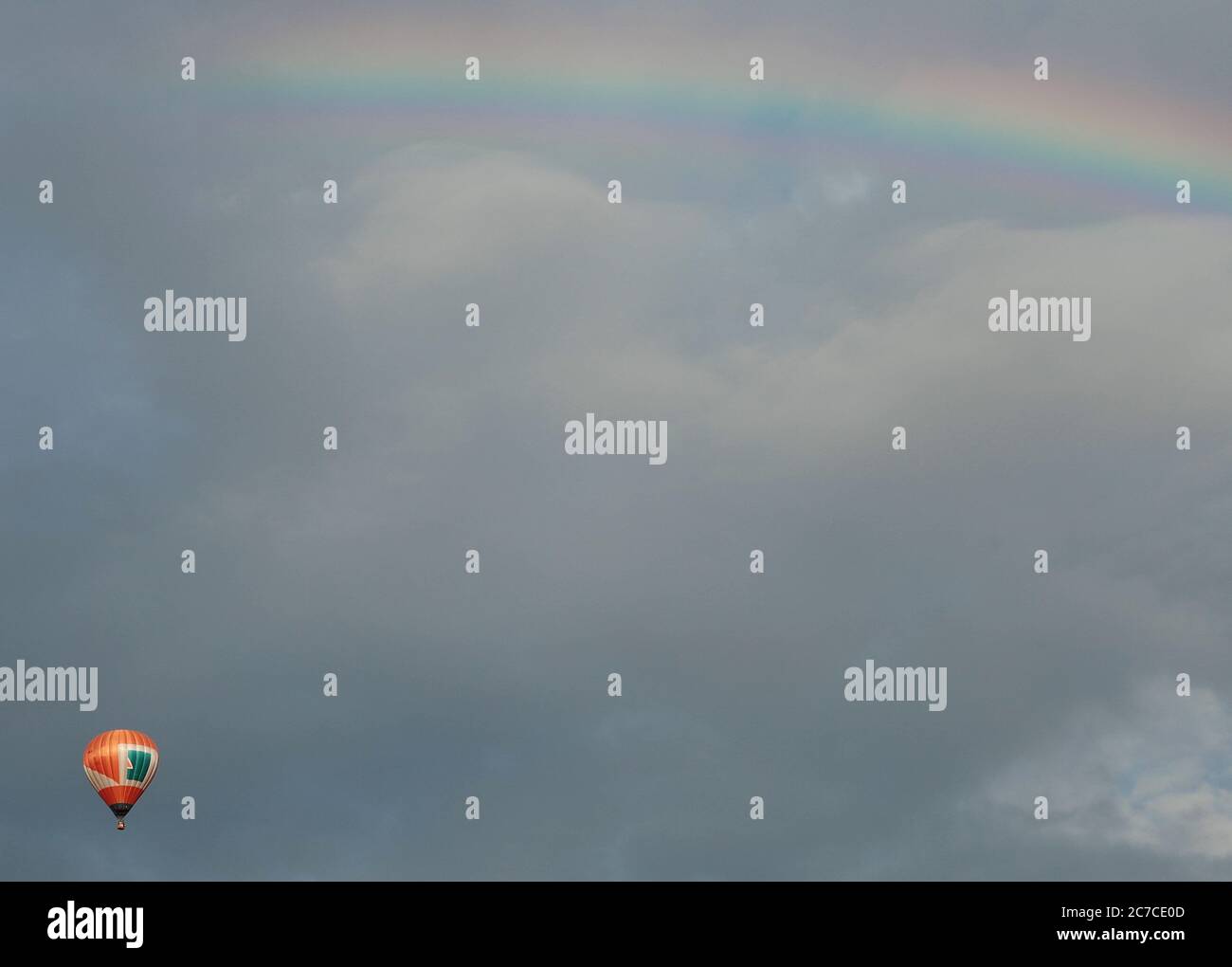 Horizontal shot of the cloudy sky with a rainbow and a hot air balloon ...