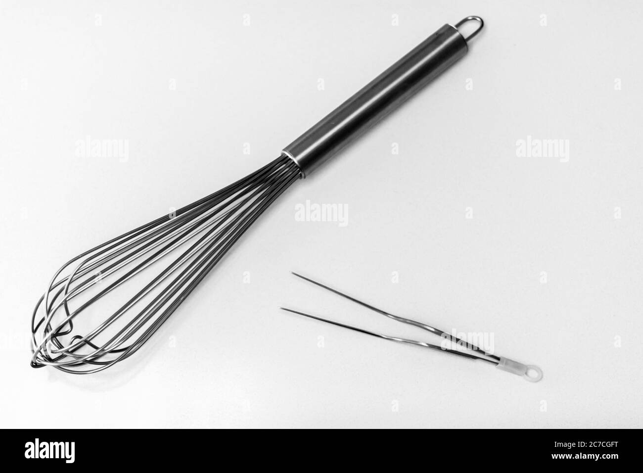 High angle greyscale shot of whisks and tongs on a white surface Stock Photo