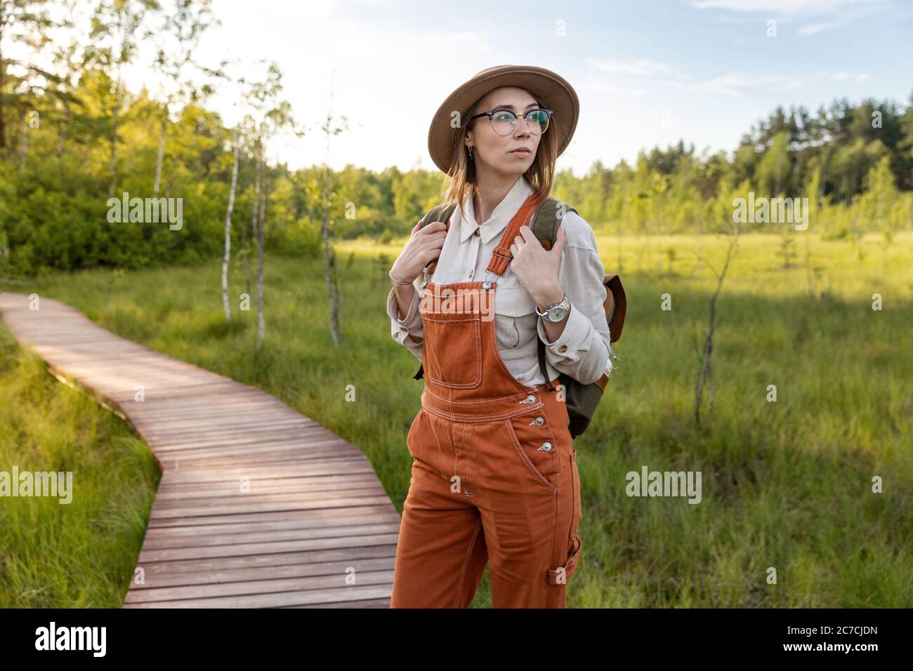 Portrait of woman botanist with backpack on ecological hiking trail in summer. Naturalist exploring wildlife and ecotourism adventure walking on path Stock Photo