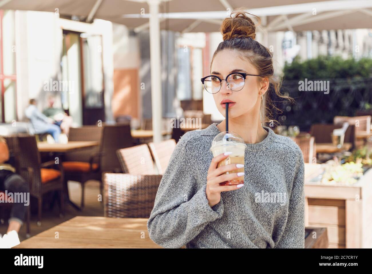 Young woman in street cafe drinks cocktail and looks away Stock Photo