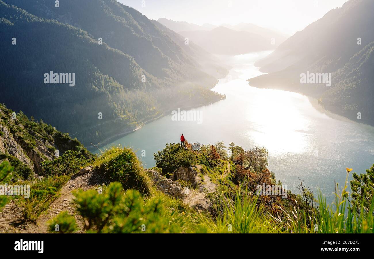 Exploring valley from top of mountain enjoying beautiful view to summer lake with turquoise water - adventure, travel and hiking concept. Plansee Stock Photo