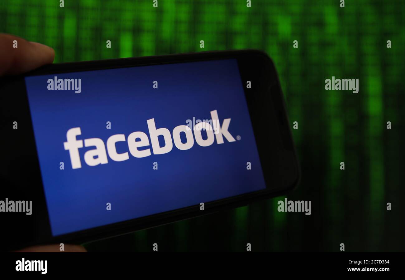 Viersen, Germany - July 9. 2020: View on mobile phone with facebook logo hold by hand. Screen with tunnel of binary code numbers background. Stock Photo