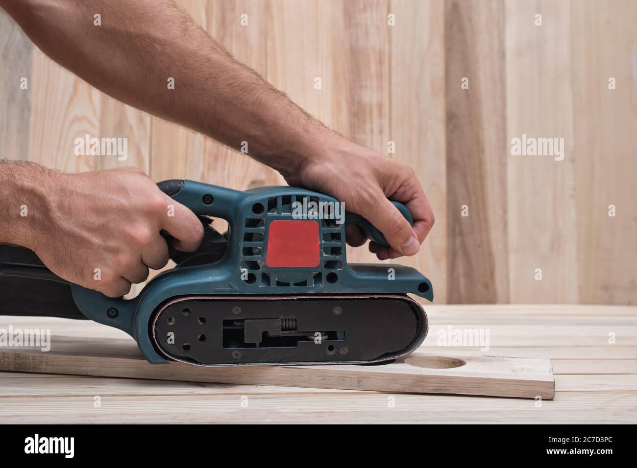 Electric belt sander sanding machine in male hand. Processing of workpiece on light brown wooden table. Side view close up Stock Photo Alamy