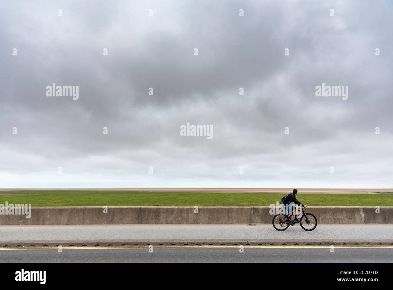 Lonely solitary cyclist rides along a deserted beachside road during Coronovirus lockdown. Stock Photo