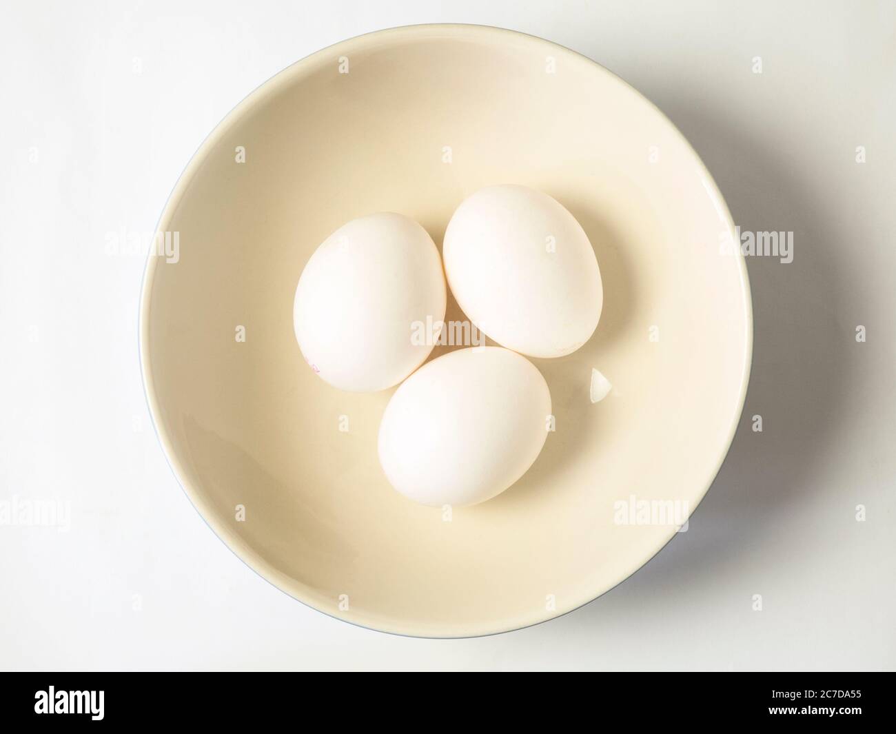 Three white eggs in a bowl centred on a white background Stock Photo