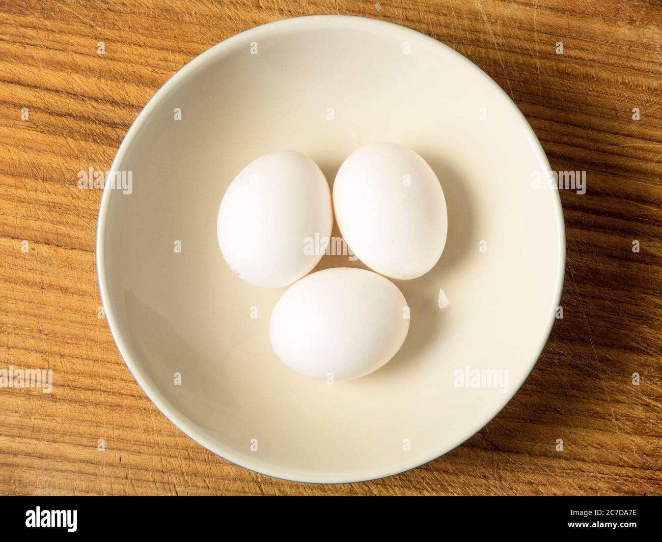 Three white eggs in a bowl centred on a wooden chopping board Stock Photo