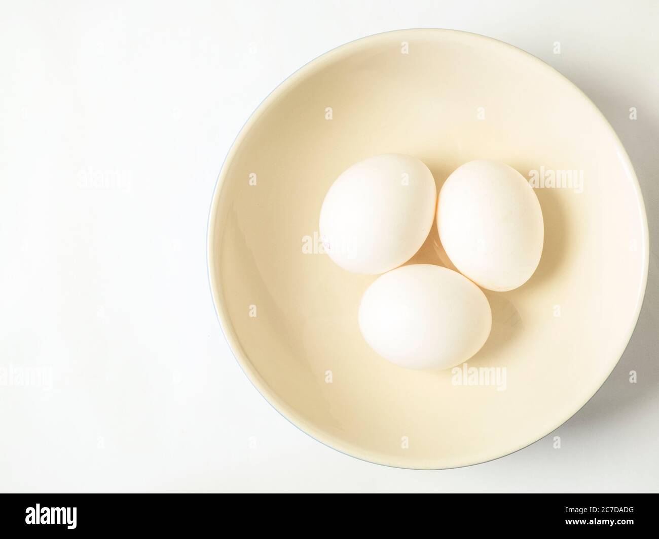 Three white eggs in a bowl offset on a white background with copy space Stock Photo