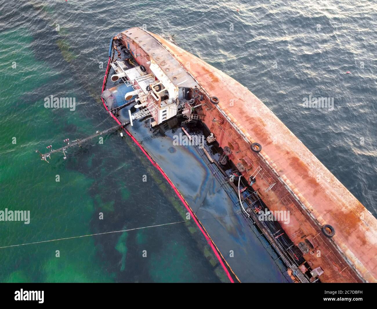 An overturned rusty tanker ran aground. Environmental disaster and oil spill into the sea by the sea. Old ship on the background of the emerald sea. Stock Photo