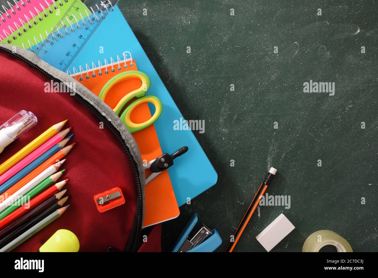 Detail of backpack full of school supplies on green blackboard. Top view Stock Photo