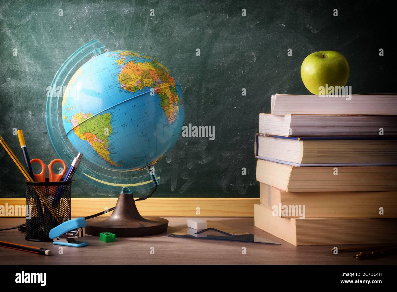 Stack of books and school supplies on classroom desk with green ...