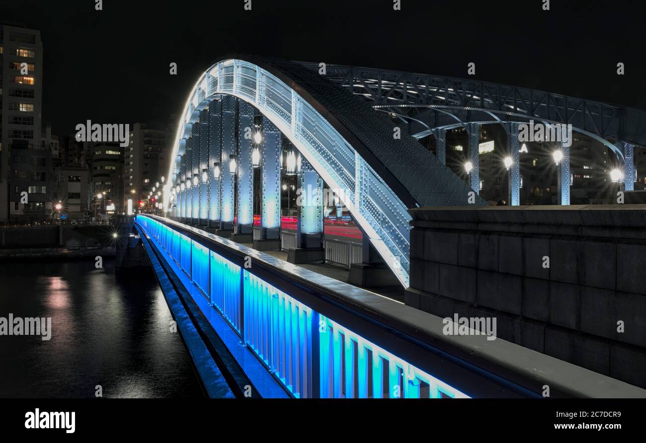Night view from one end of an urban bridge illuminated in blue with an arch curving over it Stock Photo