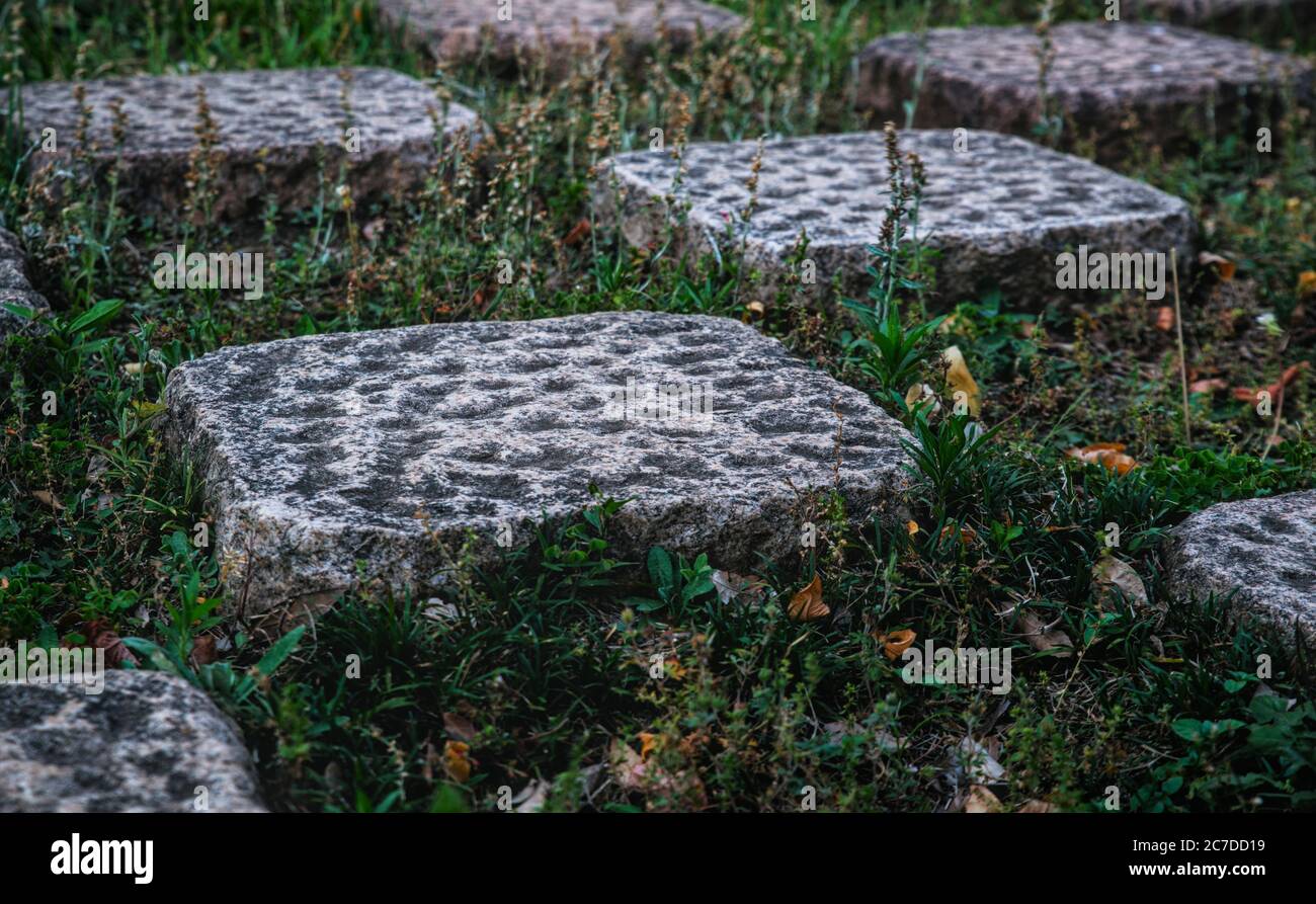 Sidelong perspective of a checkered pattern of dimpled stone tiles and square patches of grass with bits of leaf litter visible Stock Photo