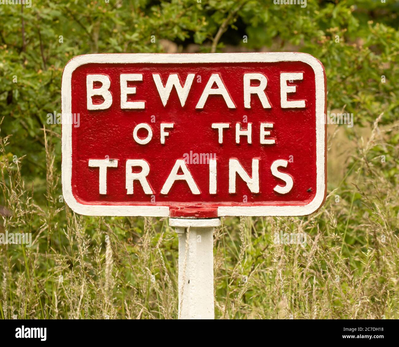 Beware of the Trains sign, cast iron - red with white lettering, against a grassy background Stock Photo